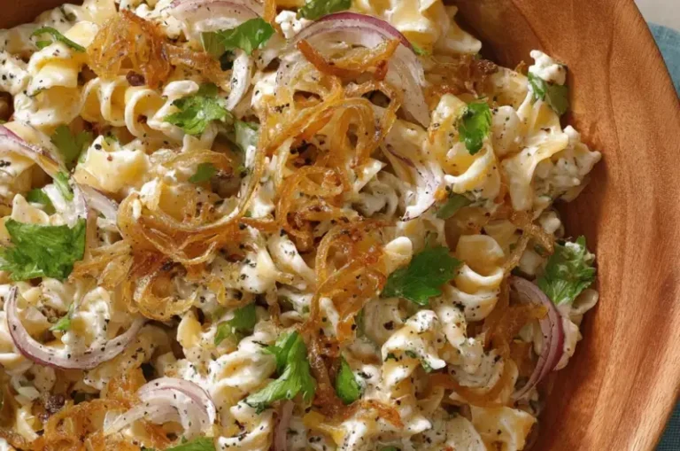A bowl of French Onion Pasta Salad with onions, cheese, and herbs garnished on top.