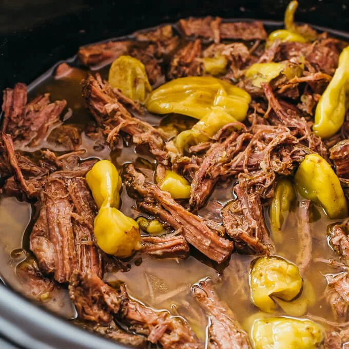 Slow cooker pot roast with colorful peppers and herbs served in a rustic dish