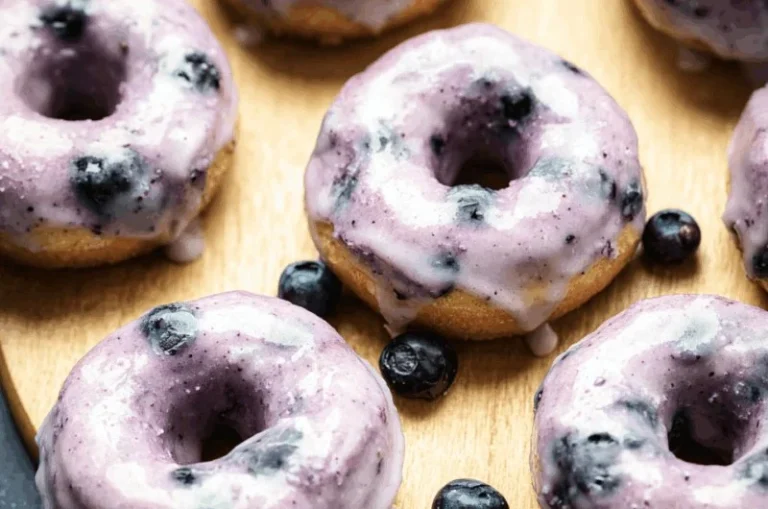 Freshly baked blueberry cake donuts topped with icing and blueberries