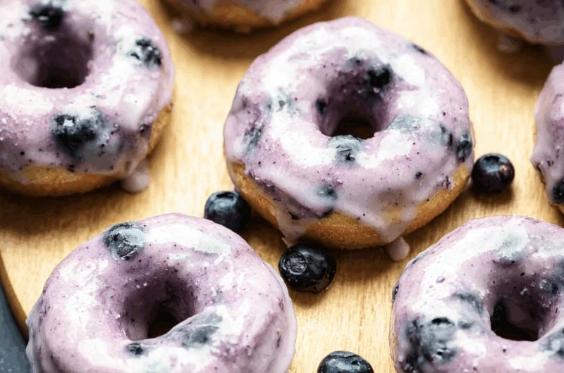 Freshly baked blueberry cake donuts topped with icing and blueberries