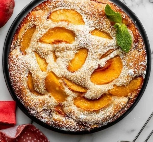 Freshly baked peach cake topped with slices of ripe peaches and whipped cream